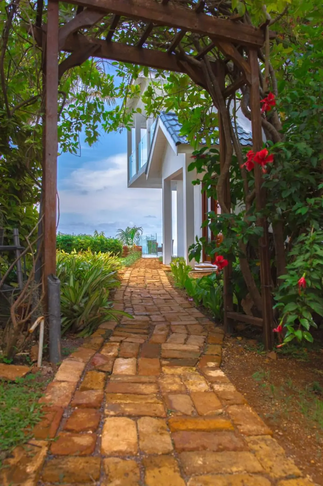 Brick garden pathway beneath a leafy wooden arch.